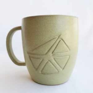 A handmade large green ceramic mug with handle and carved Aboriginal motif on front