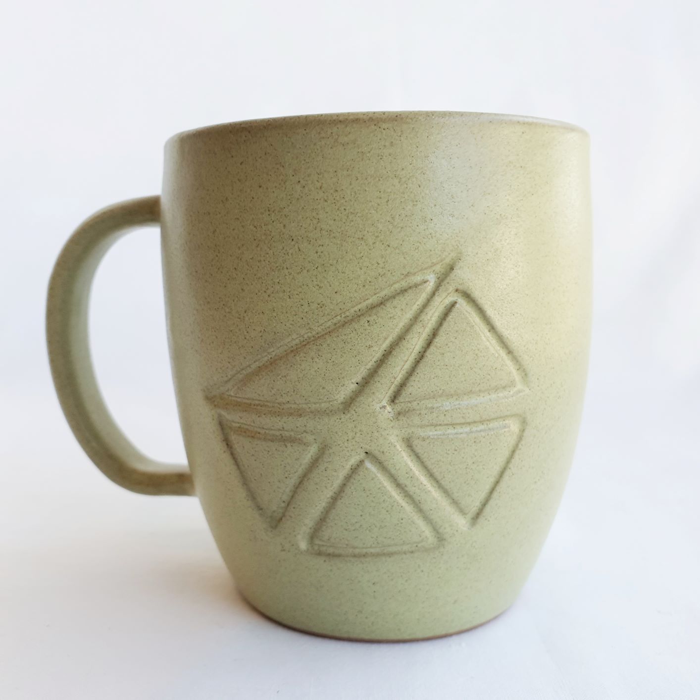 A handmade large green ceramic mug with handle and carved Aboriginal motif on front