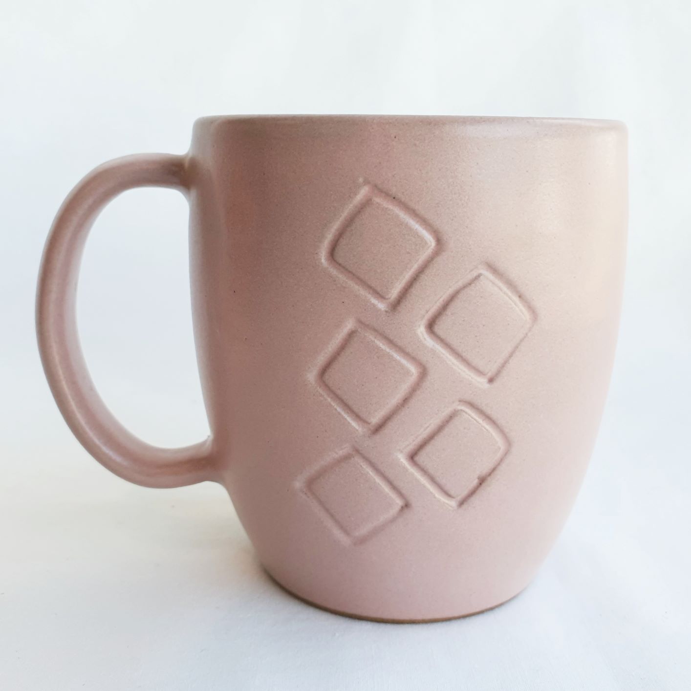 A handmade large pale pink ceramic mug with handle and carved Aboriginal motif on front